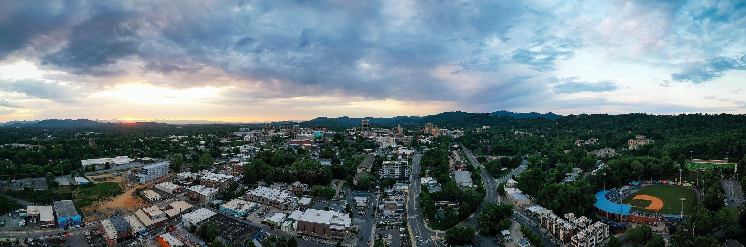 Aerial panorama of downtown Asheville, North Carolina at sunset, with the Blue Ridge Mountains behind the skyline
