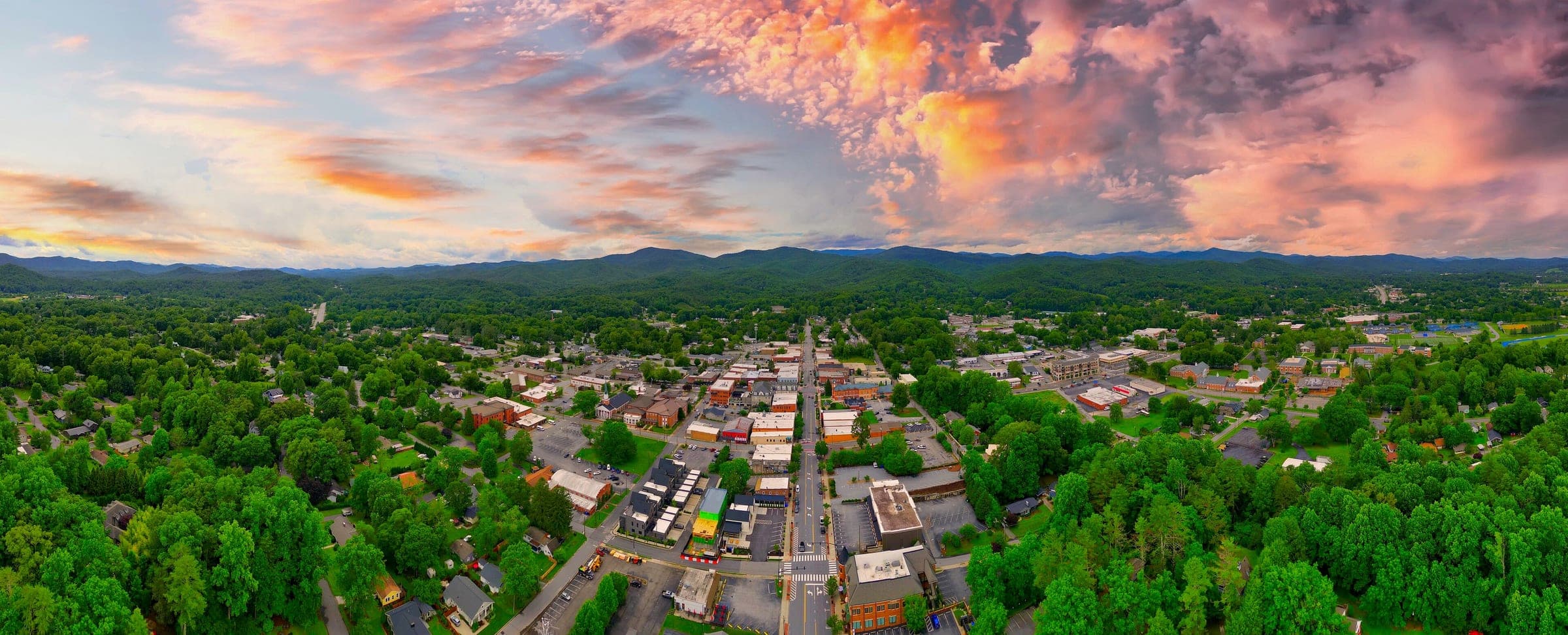 Aerial panorama of downtown Brevard, North Carolina at sunset, with pink clouds over the surrounding forested ridges